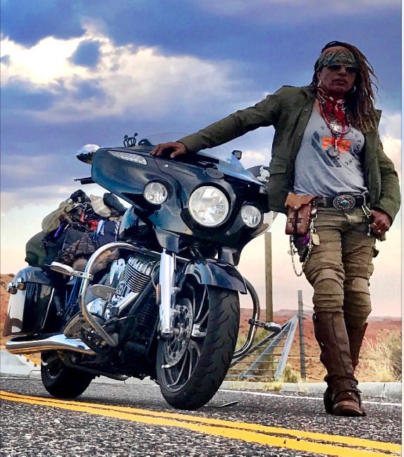 Gevin standing beside her Indian motorcycle on the road